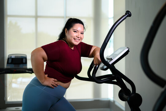 Portrait of young Asian overweight women exercising on elliptical trainer in the gym. Weight loss workout, healthy lifestyle concept. - Powered by Adobe