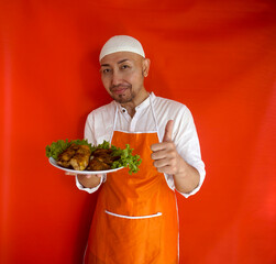 Smiling Asian Male Chef Serving Chicken Dish Holding Plate Showing Thumb Up Standing On Red Background. 