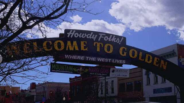 Welcome sign downtown Golden Colorado winter clouds shade blue sky Denver Front Range suburb city Boulder Lookout Mountain Table Mountain Clear Creek tree business slide left motion