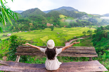 Young happy woman tourist enjoying and relaxing with beautiful landscape view rice paddy field while traveling at Nan, Thailand