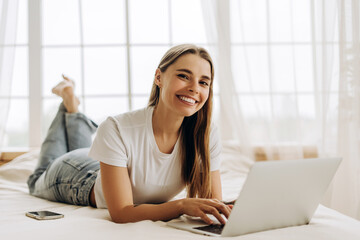 Smiling woman lying on bed using laptop and working remotely from home