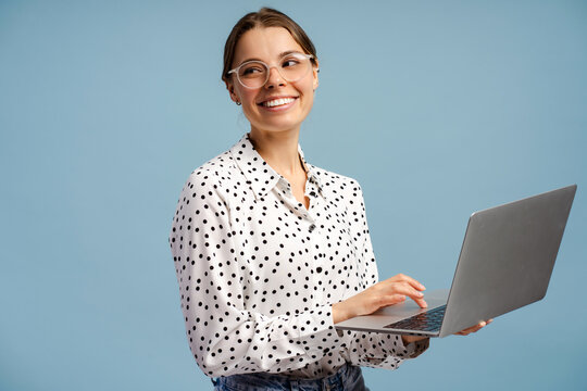 Smiling businesswoman using laptop and looking away on blue background