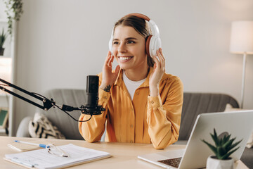 Happy female radio host wearing headphones recording podcast in home studio