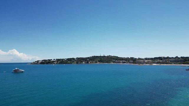 View of the Cote d'Azur featuring the Ch&acirc;teau Grimaldi and Mus&eacute;e Picasso in Antibes, France. The scene includes a clear blue sky and calm turquoise waters.