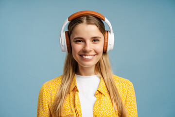 Smiling blonde woman wearing headphones listening to music on blue background