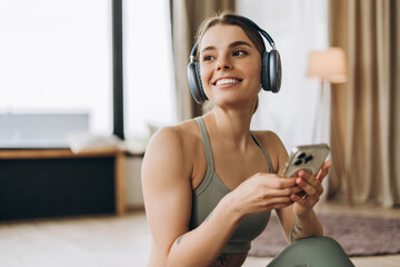 Young sportswoman wearing headphones and holding smartphone is choosing music for training