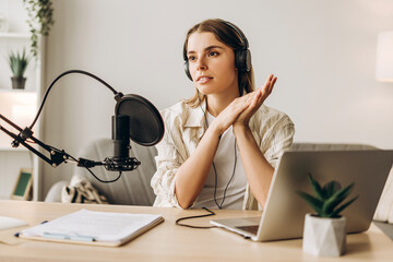 Female podcaster speaking into a microphone and recording audio at home studio