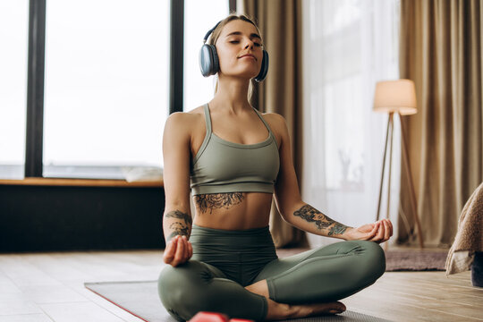 Young woman meditating with headphones in lotus position at home