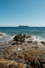 Waves washing onto the rocky coastline of the northern tip of Cap Corse on the Mediterranean island of  Corsica with the island of Giraglia in the distance