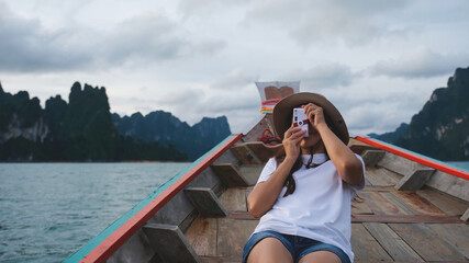 A woman sitting on a long tail boat and taking a photo while traveling on the river