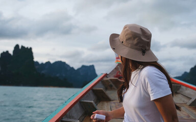 A woman sitting on a long tail boat and taking a photo while traveling on the river