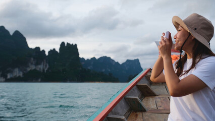 A woman sitting on a long tail boat and taking a photo while traveling on the river
