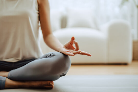 Close up hand of Asian woman practicing yoga and meditation at home sitting on floor in living room in lotus position. Mindful meditation and wellbeing concept