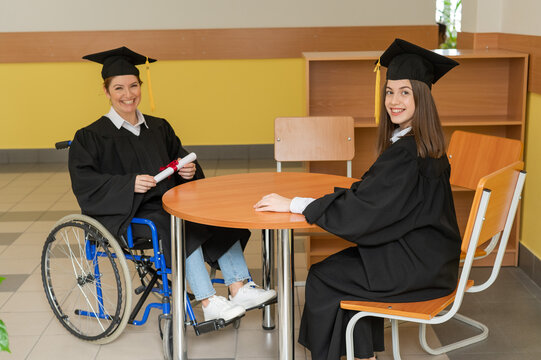 Happy young woman and woman in wheelchair in graduate gown with diploma in hands. Inclusive education.