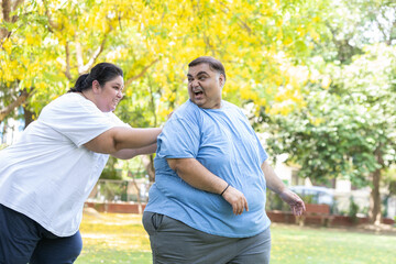 Overweight couple having fun together at summer park. Fat woman pushing man. Fat friends enjoy...