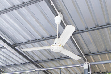 White old ceiling fan hanging on steel beams under an aluminum roof. Modern room cooling device...