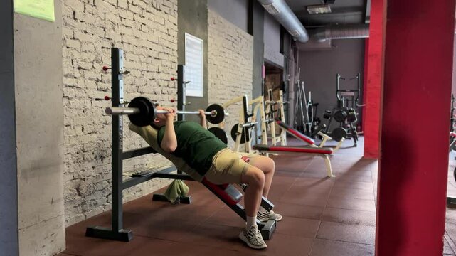 A man performs a barbell bench press in the gym. He pushes through the final exhausting set, straining to complete the reps with effort and determination.