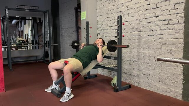 A man performs a barbell bench press in the gym. He pushes through the final exhausting set, straining to complete the reps with effort and determination.