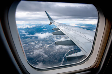 Naklejka premium View through airplane window during landing, wing visible with ground approaching, cloudy weather