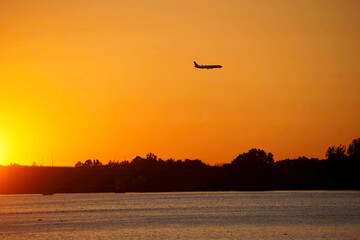 Sunset with airplane in silhouette above river 
