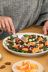  Woman eating winter salad with fresh spinach, mandarin and pomegranate at wooden table.