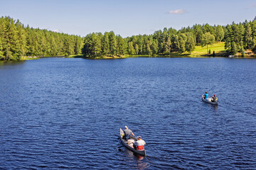 People paddling canoes on a lake in a forest on a sunny summer day