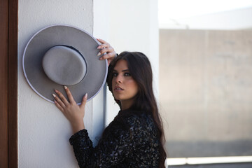 portrait of a Latin woman, young and beautiful flamenco dancer with her hands and arms on the wall holding a hat. The woman looks at the camera with a serious and sensual face