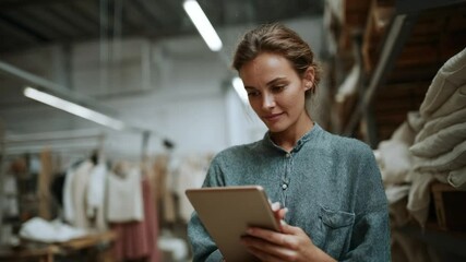 Efficiency in Textile Industry: A determined female professional in textile industry, focused on inventory and order processing, with her digital tablet in a vibrant textile warehouse. - Powered by Adobe