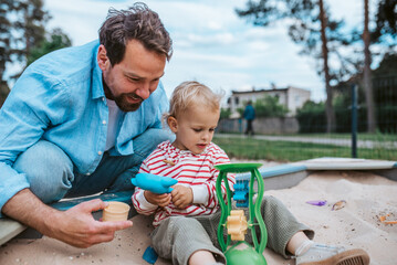 Father and little toddler son playing in the sandbox on playground.