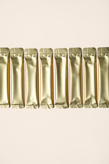 Row of Several Shiny Golden Sachets on a Light Background. Packaging for Powder Products.