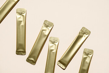 Multiple Golden Foil Stick Packs and Sachets on Beige Background. Mockup for a Quick Food Product, Skincare or Medicine.