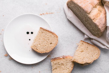 Overhead view of sliced homemade artisan bread with a plate of oil and balsamic vinegar on a white countertop, top view of baked sourdough artisan bread  and a dip on a white background