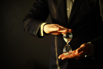 Businessman holding an hourglass isolated on dark background - time is money concept.