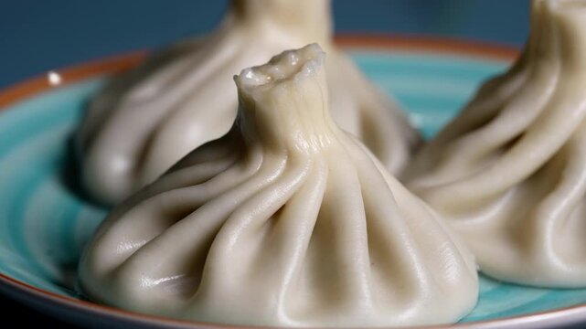 Trio of khinkali dumplings with shiny, soft dough and detailed folds, arranged on a turquoise dish.