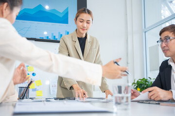 Group of confident professional business people pointing at graphs and charts to analyze marketing data to plan new sales strategies to increase productivity in modern office.