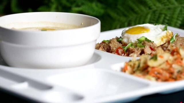 White soup bowl with creamy soup, fried rice topped with egg, and fresh salad on a white tray, green background.