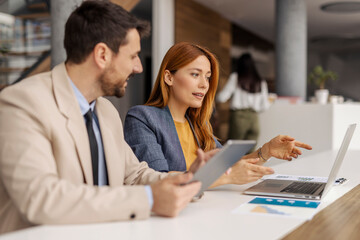 Professional female executive sitting with her coworker at corporate office and pointing at laptop while working on new business plan.