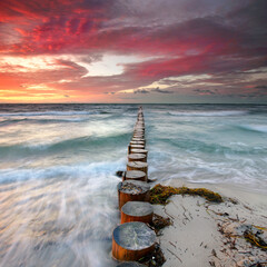 Raging Waves and red burning Skies: Weathered Wooden Groynes Amidst a Stormy Sea