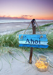 weathered sign with AHOI text in the dunes in sunset sky