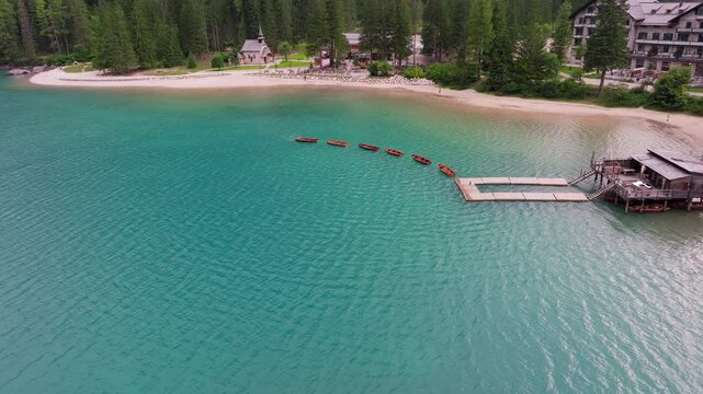 High aerial over turquoise lake in Dolomites with wooden boats and lush forest edge