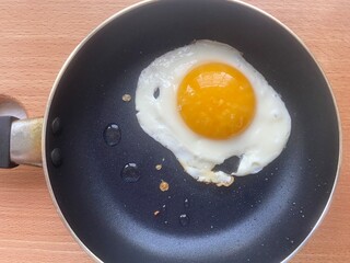 Fried egg in a non-stick frying pan on wooden background, close-up of breakfast cooking, sunny side up egg, simple home-cooked meal