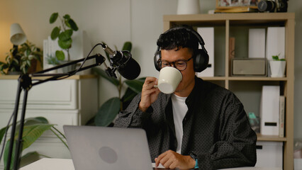 Asian man hosts a business podcast from his home studio while sipping coffee.