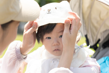 お母さんに帽子をかぶせてもらっている赤ちゃん