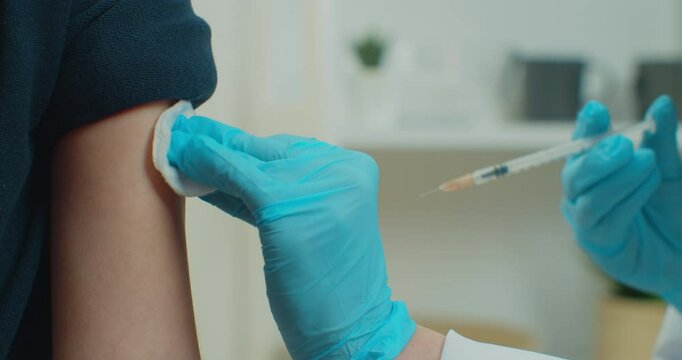 Close up of little child patient sitting in mask at home during coronavirus while professional doctor hands in uniform and gloves making injection vaccinating kid. Vaccination concept.