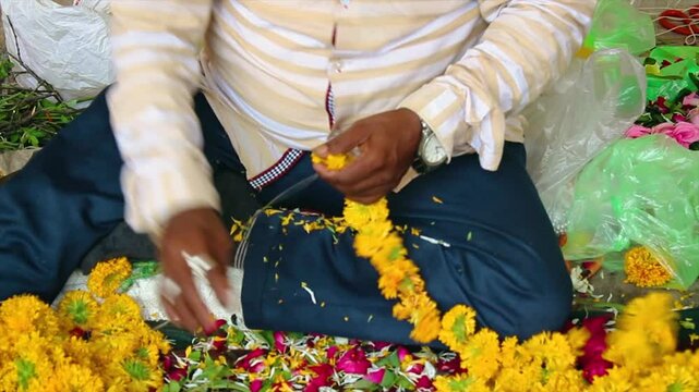 Close-up of man making marigold flower garland for temple, wedding or festival. Indian tradition and handmade work. Great for culture, rituals or craft videos.
