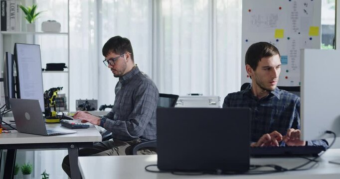 Adult male engineer team discusses AI software development robotic hand project use AI code solutions at tech workspace. Artificial intelligence interface, collaboration support prototype development.