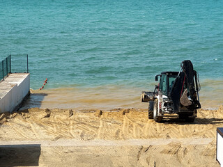 Beach construction with bulldozer preparing sandy shore for coastal restoration, maintenance, and tourism infrastructure development