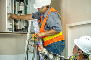 Technician Conducting Electrical Maintenance Work Inside Control Panel Using Multimeter and Testing Equipment While Wea Safety Helmet and High-Visibility Vest