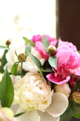 A vibrant arrangement of pink and white peonies sits in a warm, well-lit indoor space, showcasing the lush petals and fresh greenery. Sunlight enhances the colors.