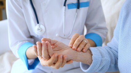 Female doctor measuring the pulse of a senior woman during a home visit, delivering compassionate...